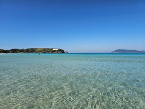 A clear coastal view with a building on a hill, calm sea, and a boat in the distance. - O AP mais lindo da Praia do Forte 213 (Cabo Frio)