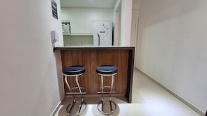 A narrow kitchen with a wooden countertop, two bar stools, and a refrigerator. - O AP mais lindo da Praia do Forte 213 (Cabo Frio)