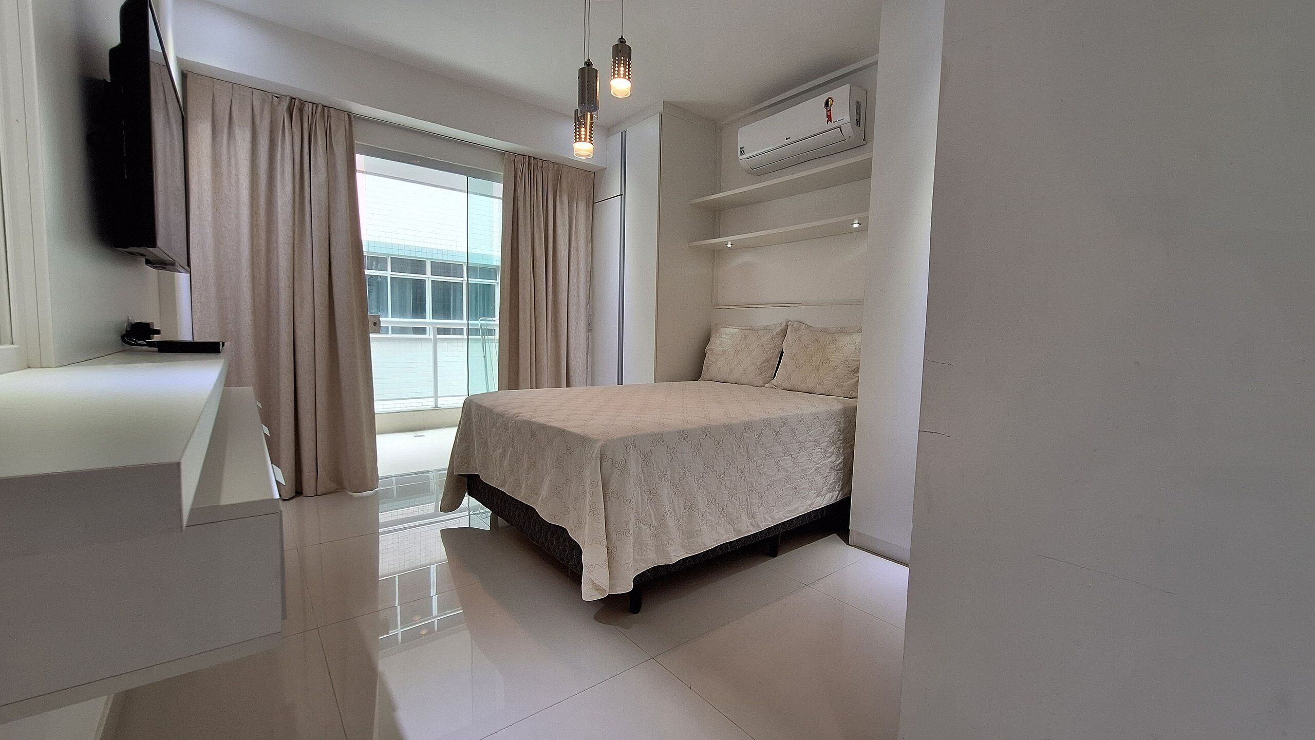 Un dormitorio con cama, televisión, ventana con cortinas y balcón.