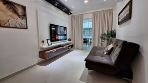 A modern living room with a flat-screen TV, a sofa, a coffee table, and a dining area visible through a glass door. - O AP mais lindo da Praia do Forte 213 (Cabo Frio)