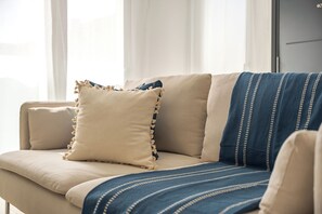 Ein beiges Sofa mit einer blau-weiß gestreiften Decke und einem dekorativen Kissen mit Fransen.