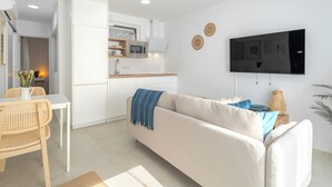 A modern living space with a sofa, a dining table, a kitchen area, and a flat-screen TV mounted on the wall. - Charming 2-bedroom Apartment in Guargacho, Tenerife (Arona)