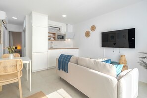Ein moderner Wohnraum mit Sofa, Esstisch, Küchenzeile und flachbildschirmfernseher an der Wand.