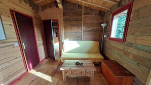 A wooden cabin interior with a bed, a table, and a lamp.