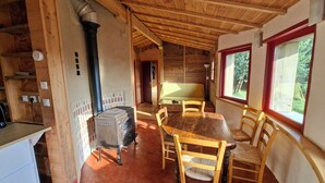 A wooden cabin interior with a dining table, chairs, a radiator, and a window with a view.