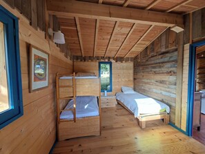 L’intérieur d’une cabane en bois, avec des lits superposés, une échelle, une petite table et une fenêtre.
