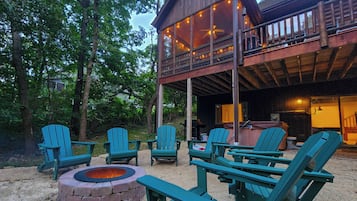 A wooden deck with Adirondack chairs and a fire pit, surrounded by trees.