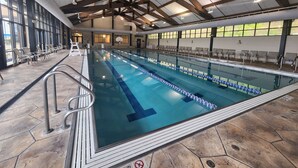 Ein Hallenbad mit deutlich abgegrenzten Bahnen, einer Holzbalkendecke und einem Sitzbereich mit Stühlen.