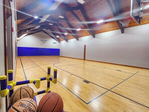 Una cancha de baloncesto interior con suelo de madera, aro de baloncesto y pared acolchada azul.