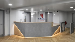 Bancada de recepção com logotipo, piso de madeira em padrão herringbone e iluminação pendente.