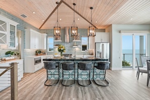 A modern kitchen with a central island, hanging pendant lights, and a view to the outside. - New! Beachfront, Heated Pool, Hot Tub & Golf Carts (North Captiva)