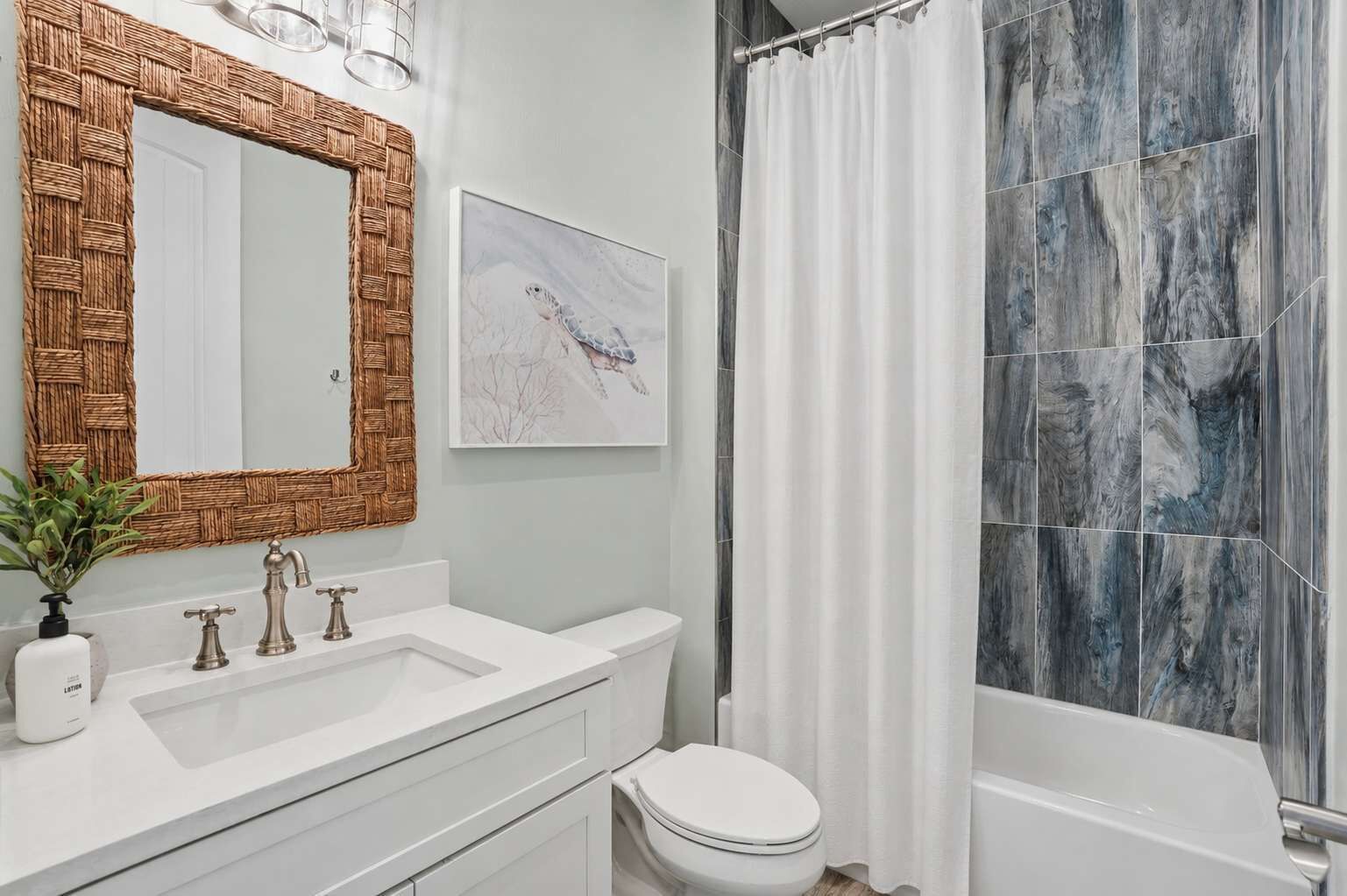 Une salle de bain avec un lavabo blanc, un miroir avec un cadre tressé, des toilettes et une douche avec un rideau.