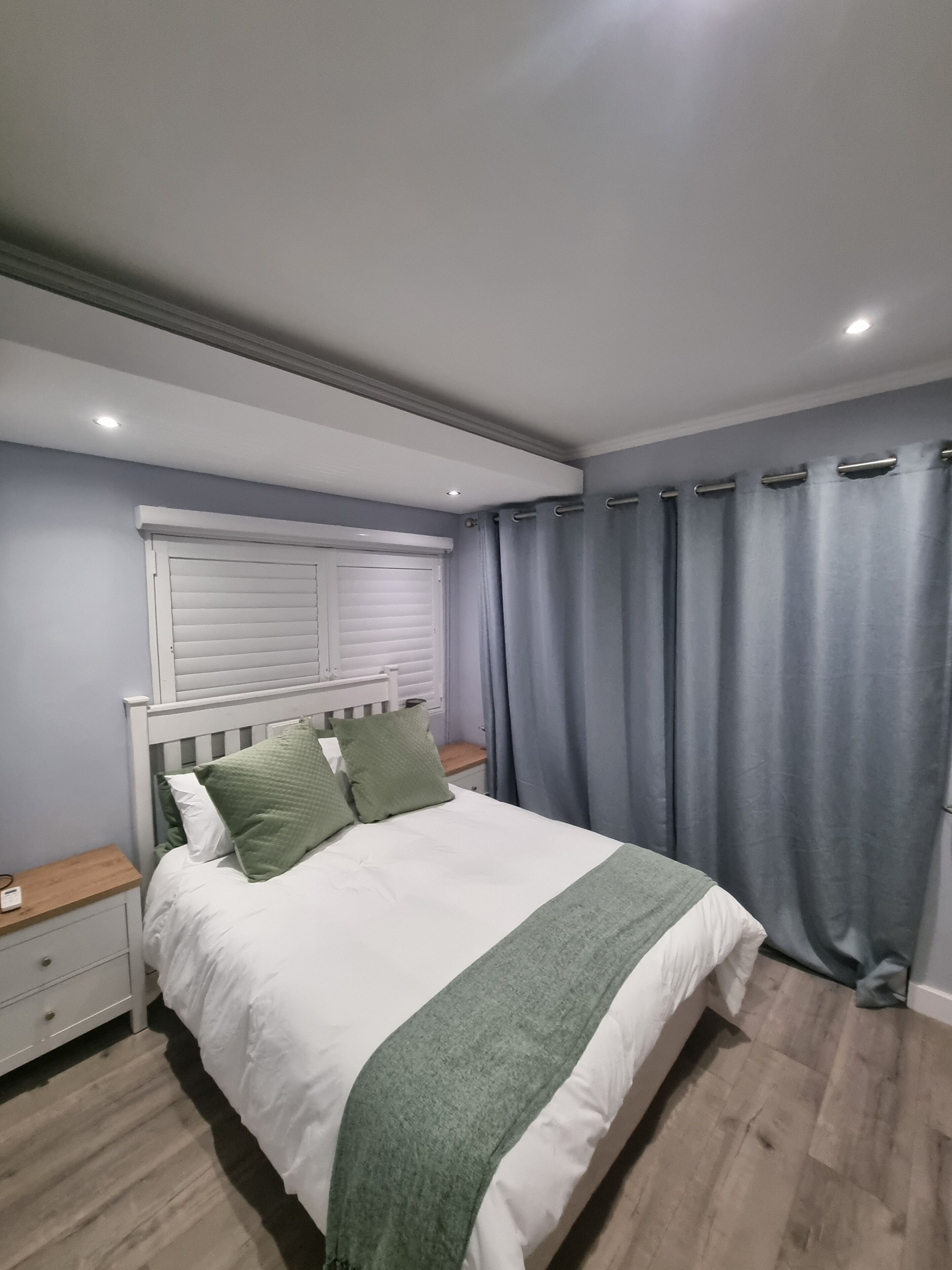 A bedroom with a bed, nightstands, a window with blinds, and grey curtains.