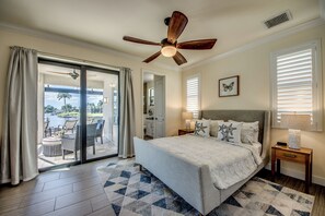 Ein Schlafzimmer mit Bett, Deckenventilator, Blick auf einen Pool und einem Fenster mit Jalousien.