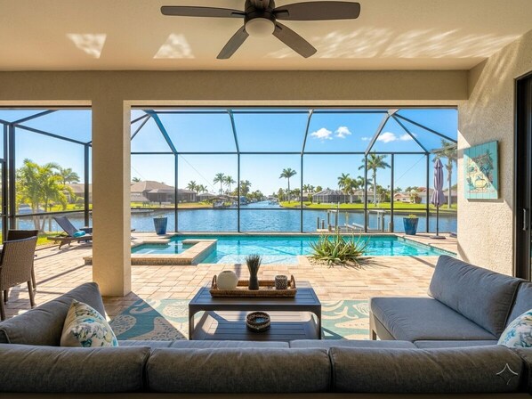 Zona de piscina con vista al agua, un ventilador de techo y un área de estar con mesa.