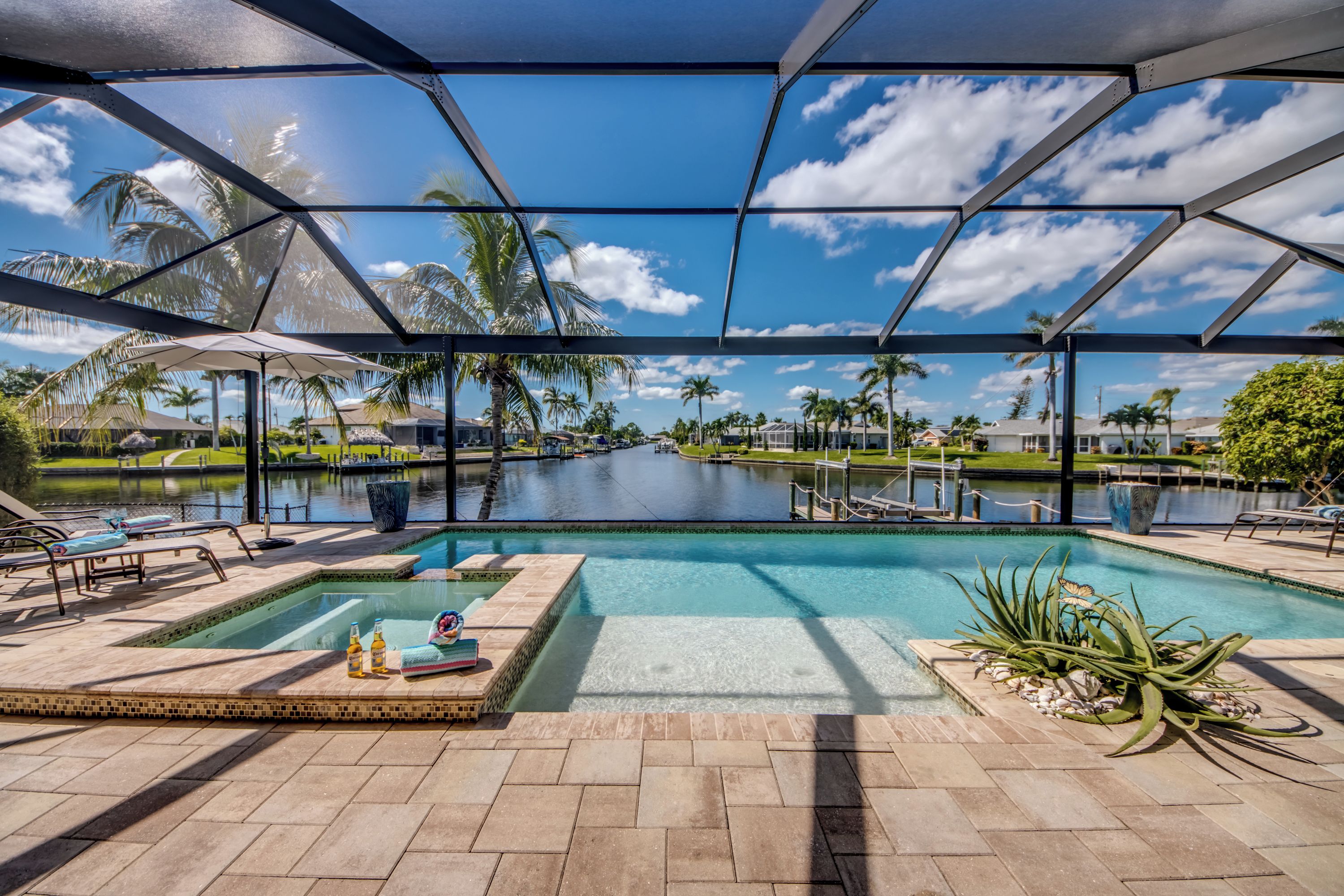 Zona de piscina con cielo despejado, palmeras y vista a una zona residencial.