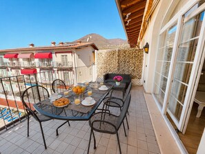 Ein Balkon mit Frühstückstisch, Sitzgelegenheiten im Freien und Blick auf die umliegenden Gebäude und Berge.