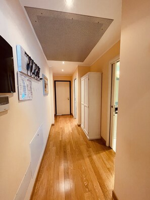 Ein Flur mit Holzboden, einem Deckenventilator, einer Tür und einem an der Wand befestigten Fernseher.