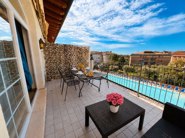 Ein Balkon mit Frühstückstisch, einem Pool und Blick auf Gebäude.