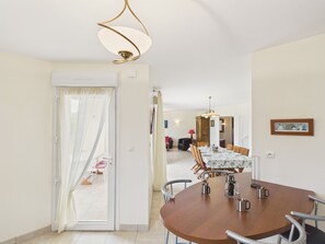 A dining area with a round table, chairs, and a hanging light fixture. - Near beach, spacious house with garden (Plouguerneau)