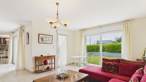 A living room with a sofa, a wooden coffee table, a dining table, and a chandelier. - Beach at 200m, family house for 7 with garden (Plouguerneau)