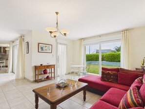 A living room with a sofa, a wooden coffee table, a dining table, and a chandelier. - Near beach, spacious house with garden (Plouguerneau)