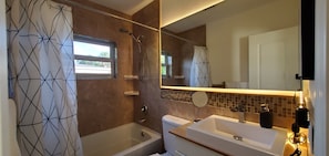 Ein Badezimmer mit Badewanne, Dusche, Toilette, Waschbecken, Spiegel und Fenster.