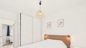 Een slaapkamer met een bed, een hanglamp en twee foto’s in lijsten aan de muur.