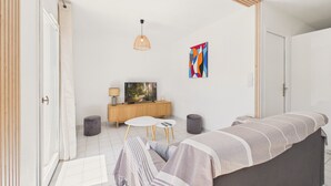 Een moderne woonkamer met een bank, een televisie, een bijzettafeltje, een lamp en een kleurrijk abstract schilderij.