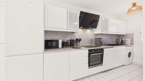 Een moderne keuken met witte kastjes, een ingebouwde magnetron, een koffiezetapparaat en een wasmachine.