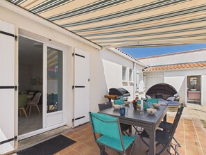 An outdoor patio with a table, chairs, a grill, and a covered area.