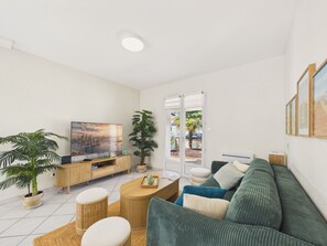 Ein modernes Wohnzimmer mit Fernseher, Sofa, Couchtisch und Blumentöpfen.