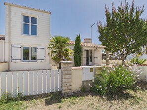 Ein zweistöckiges Haus mit weißer Fassade, einem umzäunten Garten und einer Palme.