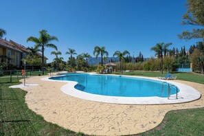 Ein Pool mit geschwungener Form, umgeben von einer gepflasterten Terrasse, Palmen und einem Gebäude im Hintergrund.