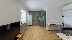Ein modernes Wohnzimmer mit Flachbildfernseher, einer Couch, einem kleinen Tisch mit Pflanze und einer Küchenzeile mit grauen Schränken und einer Marmor-Spritzschutzwand.