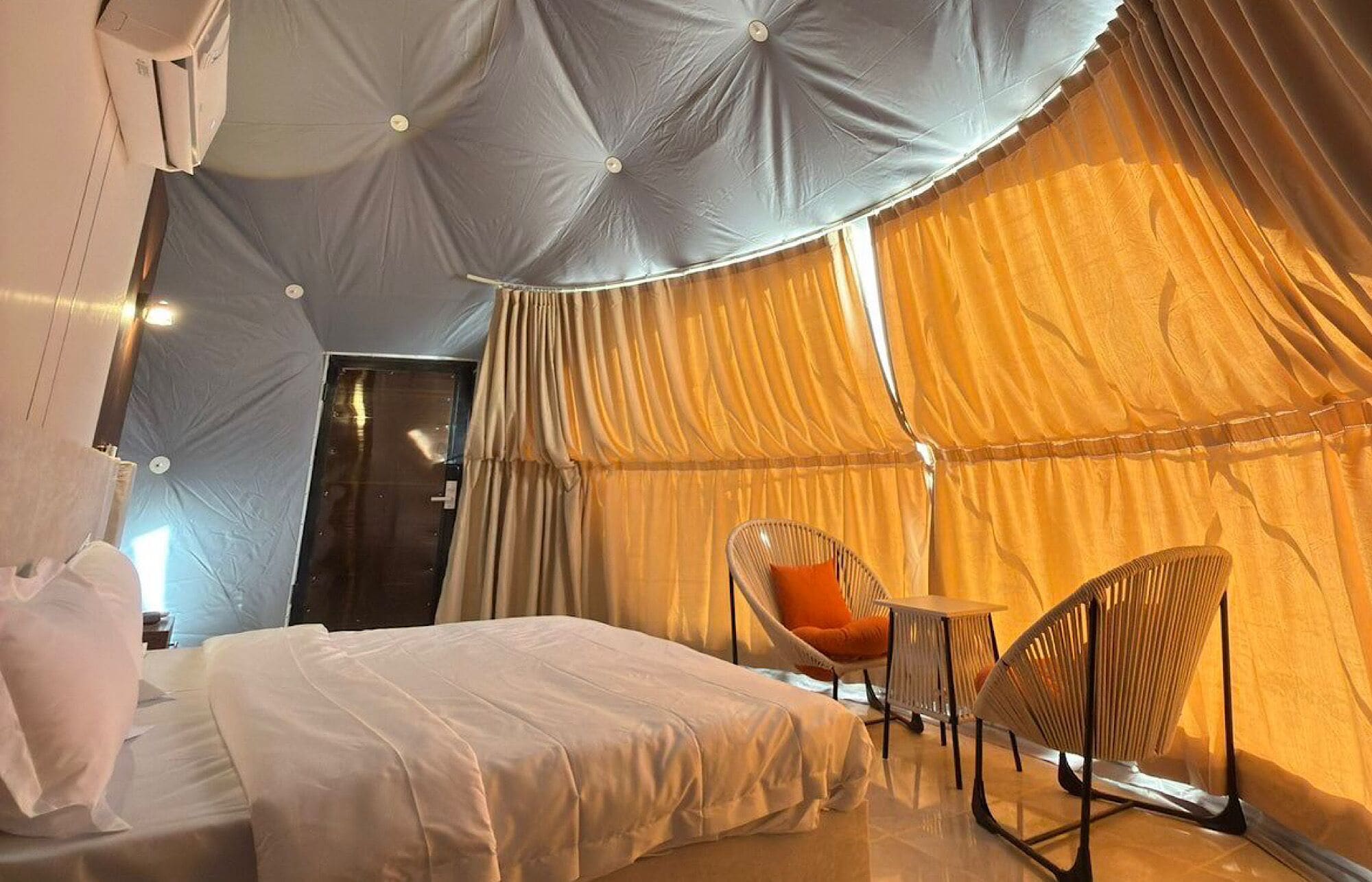 A tent-style room with a bed, two chairs, and a door.