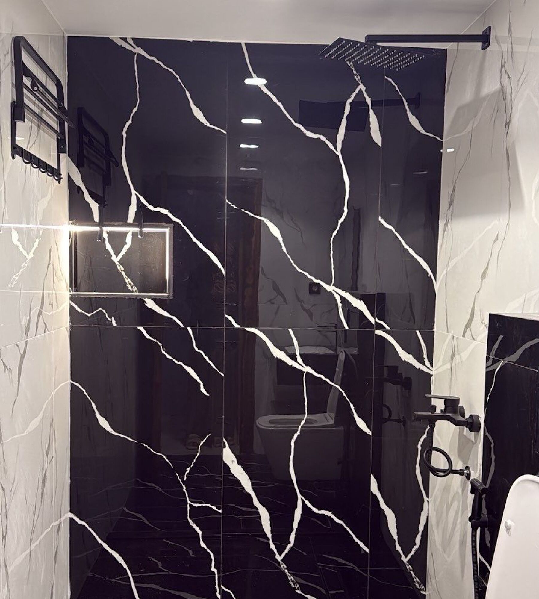 A bathroom with a black marble wall featuring white veins, a shower area, and a toilet.