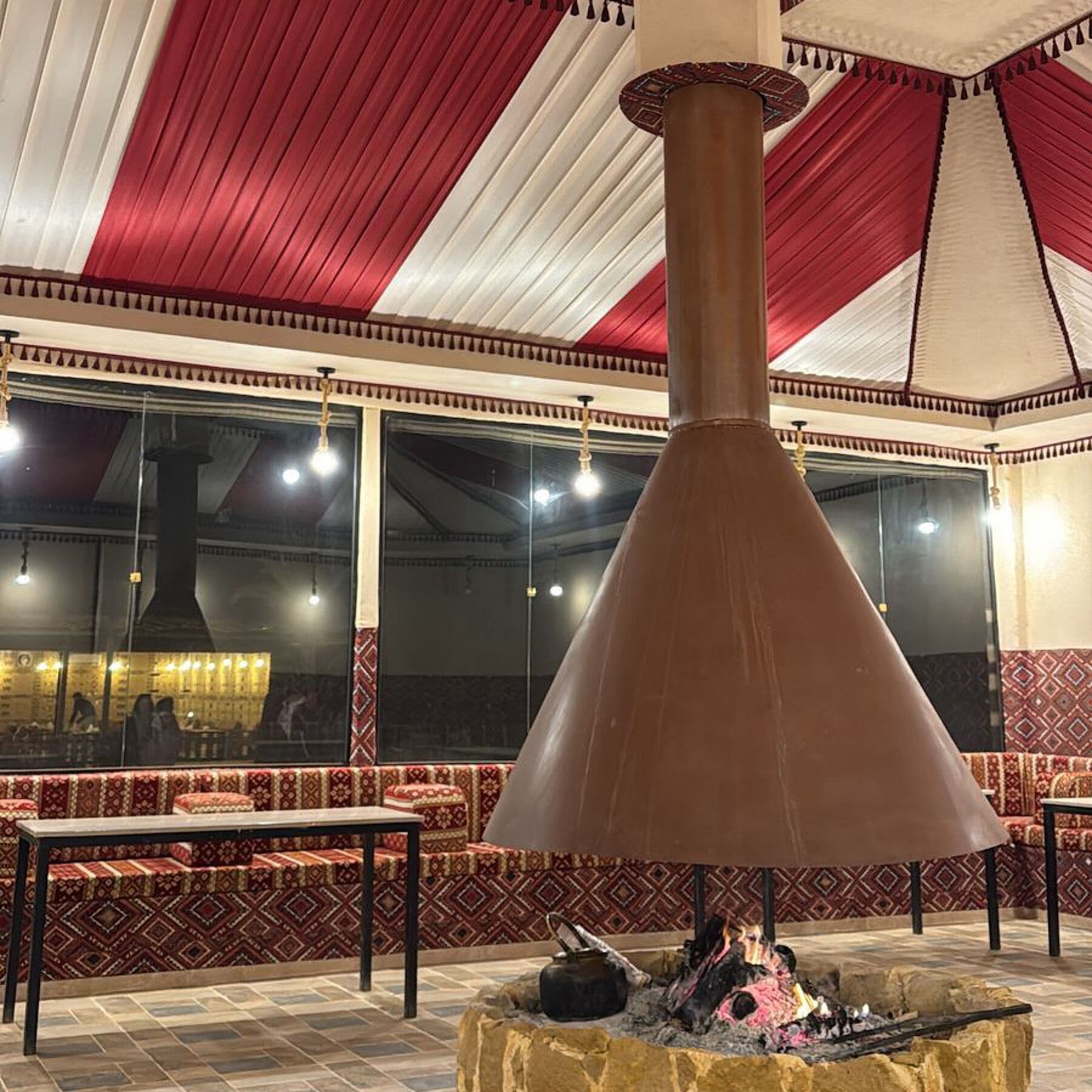 A traditional wood-fired oven in a dining area with patterned seating and a high ceiling.