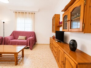 Een woonkamer met een bank, een tv op een houten kast, een lamp en een betegelde vloer.