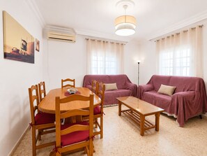 Een woonkamer met een ronde houten tafel, twee houten stoelen, een bank en een vloerlamp.