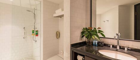 Une salle de bain moderne avec une douche à parois de verre, des toilettes blanches, un grand miroir et un plan de toilette foncé doté d’un lavabo.