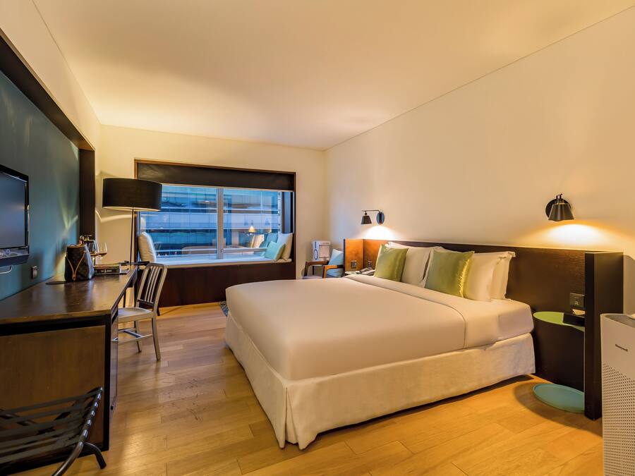 Habitación de hotel con cama, escritorio, silla, lámpara y ventana con vistas.
