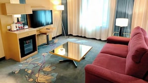 A hotel room with a television, a desk with a lamp, a red sofa, and a coffee table. - Beijing New World Centre Tongpai Hotel (Beijing)