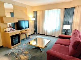 Une chambre d’hôtel équipée d’une télévision, d’un bureau avec une lampe, d’un canapé rouge et d’une table basse.