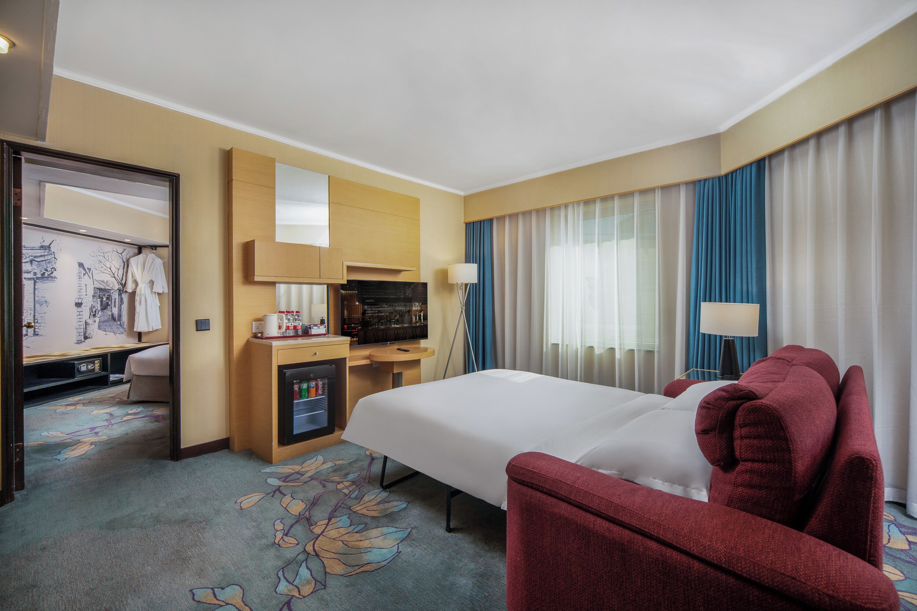 Una habitación de hotel con cama, escritorio con ordenador, televisor y minibar.