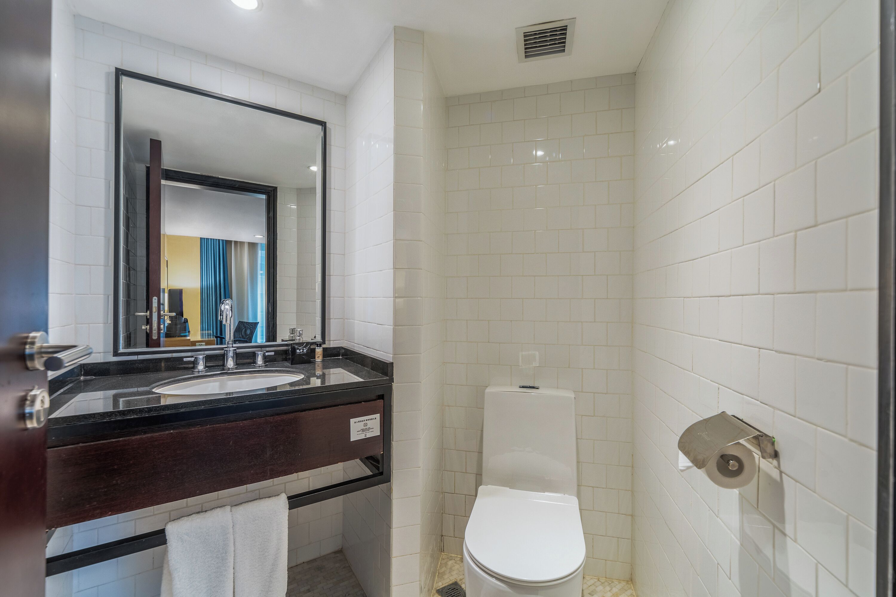 A bathroom with a double sink, a toilet, and a mirror.