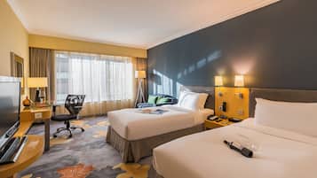 A hotel room with two beds, a desk with a computer, a TV, and a window with curtains.