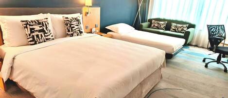 A hotel room with two beds, a green sofa, a desk, and a chair.