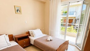 Et hotelværelse med to senge, et lille bord, en stol, et billede på væggen og en skydedør til en balkon.