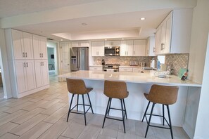 Een moderne keuken met een centraal eiland, barkrukken, roestvrijstalen apparatuur en witte kasten.